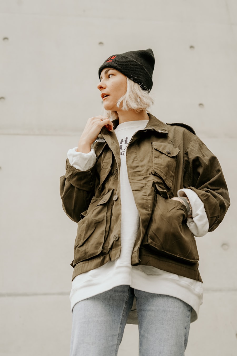 Persona con chaqueta caqui y gorro apoyada en una pared